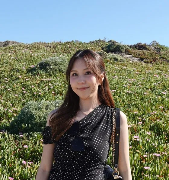 Juwita Jessica Pangestu smiling on a grassy hillside under a blue sky